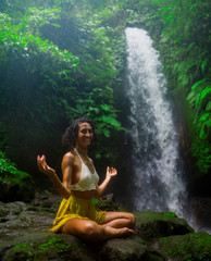 outdoors portrait of young attractive and happy hipster girl doing yoga at beautiful tropical waterfall meditating enjoying freedom and¡ nature in wellness and zen lifestyle