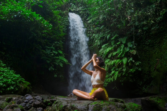 outdoors portrait of young attractive and happy hipster girl doing yoga at beautiful tropical waterfall meditating enjoying freedom and¡ nature in wellness and zen lifestyle