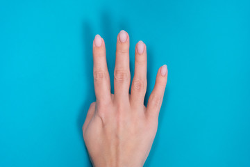 Beautiful female manicured hand isolated on blue background showing four fingers up.