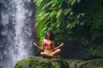 outdoors portrait of young attractive and happy hipster girl doing yoga at beautiful tropical waterfall meditating enjoying freedom and¡ nature in wellness and zen lifestyle