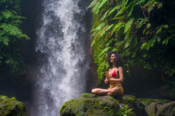 Fototapeta na wymiar outdoors portrait of young attractive and happy hipster girl doing yoga at beautiful tropical waterfall meditating enjoying freedom and¡ nature in wellness and zen lifestyle