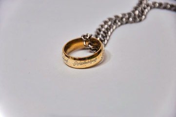 Golden ring with chrome chain on white surface. - obrazy, fototapety, plakaty