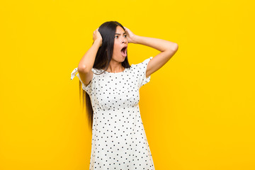 young pretty latin woman with open mouth, looking horrified and shocked because of a terrible...