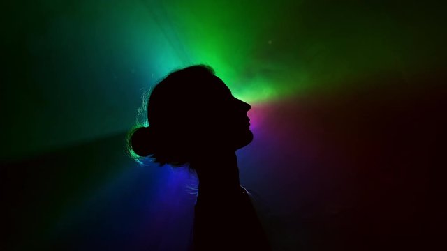 Projector. Image Of Young Girl On Light Background Of Different Colors Moving In The Dark.