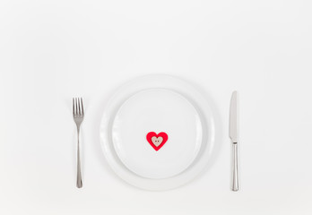 Red heart on a white plate. Valentines day or romantic dinner background. Festive romantic table setting on a white background. Valentine's card.