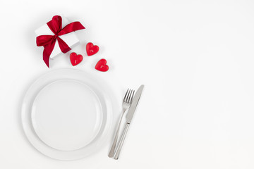Valentines day or romantic dinner background. Festive romantic table setting with candles in the shape of hearts and a gift on a white background.