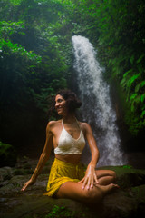 outdoors portrait of young attractive and happy hipster woman doing yoga at beautiful tropical waterfall meditating enjoying freedom and¡ nature in wellness and zen lifestyle