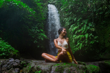 Fototapeta na wymiar outdoors portrait of young attractive and happy hipster woman doing yoga at beautiful tropical waterfall meditating enjoying freedom and¡ nature in wellness and zen lifestyle