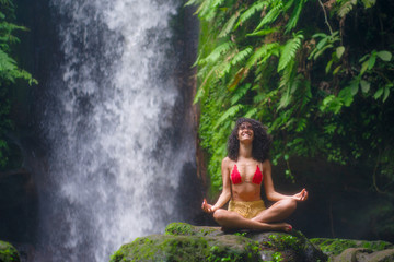 outdoors portrait of young attractive and happy hipster woman doing yoga at beautiful tropical waterfall meditating enjoying freedom and¡ nature in wellness and zen lifestyle