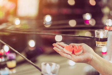 A red heart shaped candle in a woman's hand with candlelight in many small glass cups. A valentine's day background.