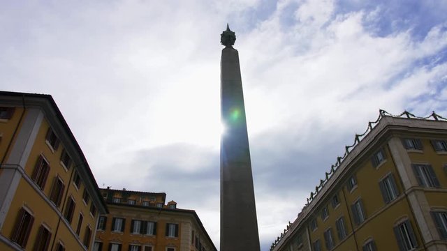 Rome, Italy - July 17, 2018: view of the obelisk standing on Piazza Montecitorio.A clear bright day, the rays of the sun break through the stella, casting off glare. On the sides are yellow buildings.