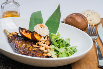 Asian cuisine, baked eggplant with nuts and rice in a deep plate on a table in a restaurant.