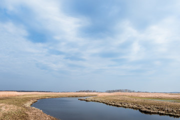 Spring landscape with a river meandering among fields under the blue cloudy sky.