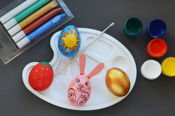 Multi-colored painted Easter eggs in the form of a rabbit, berries, sun on the desktop with paints.Idea for creativity, coloring and decorating eggs for Easter.
