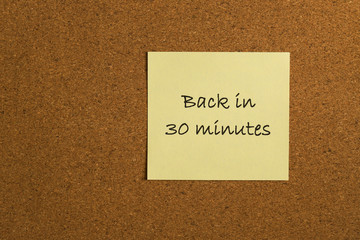 Small yellow sticky note on an office cork bulletin board with the message back in 30 minutes