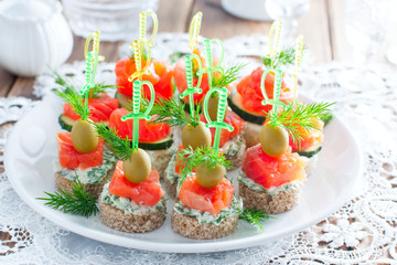 assorted canapes with salmon on white and black bread on a white plate, selective focus