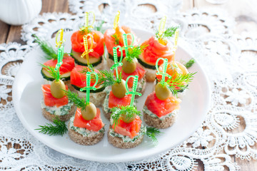 assorted canapes with salmon on white and black bread on a white plate, selective focus