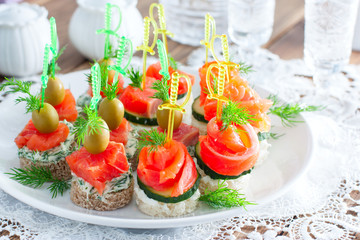 assorted canapes with salmon on white and black bread on a white plate, selective focus