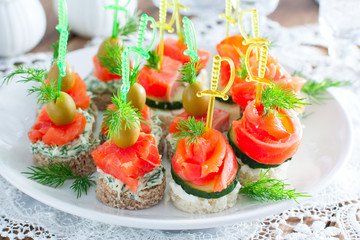 assorted canapes with salmon on white and black bread on a white plate, selective focus