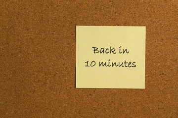 Small yellow sticky note on an office cork bulletin board with the message back in 10 minutes