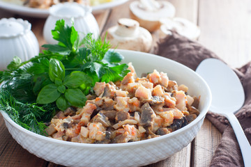 Salad with smoked chicken and fried champignons in a white plate on a wooden table with fresh...