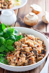 Salad with smoked chicken and fried champignons in a white plate on a wooden table with fresh herbs, selective focus