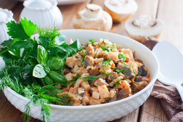 Salad with smoked chicken and fried champignons in a white plate on a wooden table with fresh herbs, selective focus