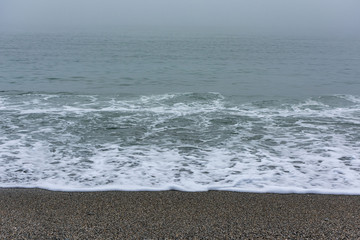 Sandy beach with the calm sea on a foggy day