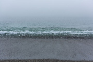 Sandy beach with the calm sea on a foggy day