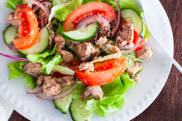 Salad with tuna and fresh tomatoes, cucumber and onions, on a white plate, selective focus