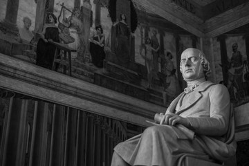 Statue of a man sitting in a chair with a picture of women in the background