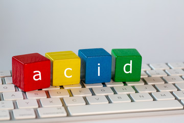 The letters acid stands for  Atomicity Consistency Isolation and Durability was written on blocks. Letters are written in white on red, yellow, blue and green blocks and stand on a bright computer