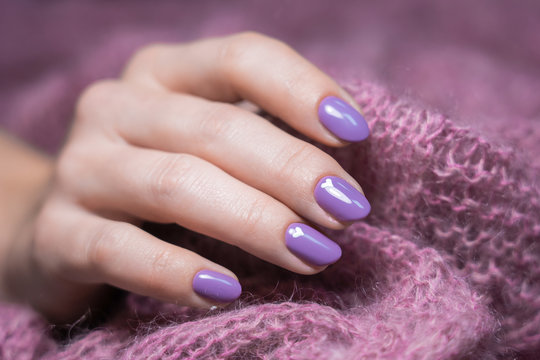 Manicured female hand isolated at soft fluffy knitted background. Fingernails with purple painted nails decorated with drawn white cute small hearts.
