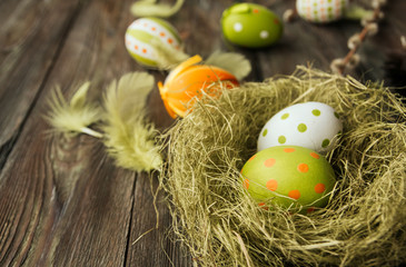 Obraz premium Green and orange easter eggs in a sisal nest on a wooden background copy space. Painted eggs. Bird feathers. Easter decoration.