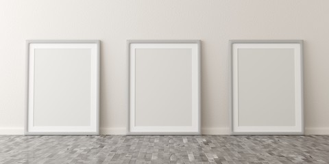 Empty picture frames leaning against white wall in bright room with wooden floor with copy space - portfolio, gallery or artwork template mock up - 3D illustration
