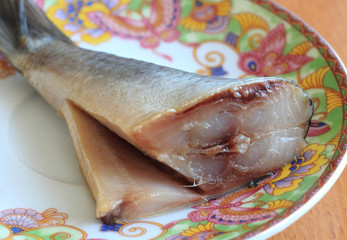 On a saucer with multicolored patterns lies a fat tail of salted herring