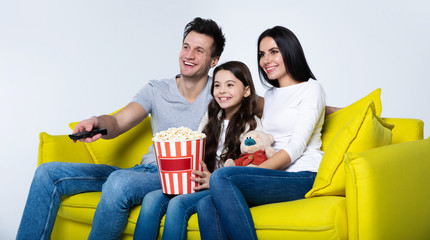 Switching channels. Young handsome man with remote control switching channels while sitting on a couch with his beautiful family.