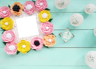 Decorative frame with colorful felt flowers and white balls of thread. Top view, copy space for your text on a blue wooden table. Background for Birthday, March 8, Valentine's Day