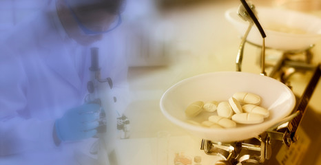 Medicine concept:  White pills on mechanical balance with a blurred background of a scientist is researching in the laboratory by microscope.
