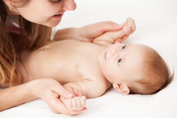Close up of adorable infant lying on soft white sheets and looking at mommy. Young woman holding tiny hands of cute newborn child. Concept of motherhood and infancy.