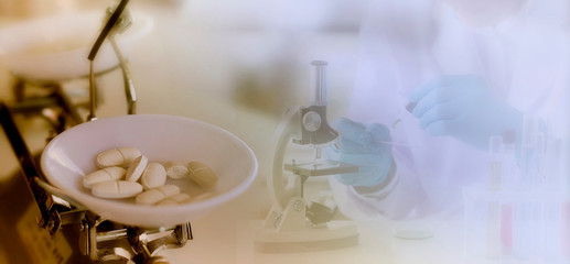 Medicine concept:  White pills on mechanical balance with a blurred background of a scientist is researching in the laboratory by microscope.