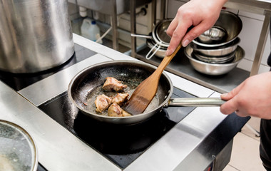 Chef cooks fried potatoes with pieces of meat in a restaurant kitchen