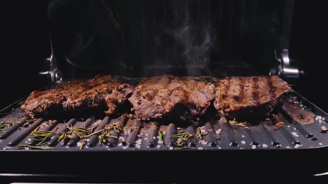 Delicious juicy meat steak cooking on grill. Silicone cooking brush. Aged prime rare roast grilling fresh marble tenderness beef. Prime beef fry on electric roaster, rosemary black pepper oil.