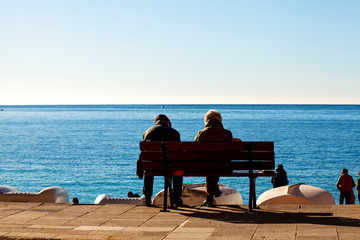 Aged couple, sitting on a bench in front of the sea, along the promenade of Camogli, take the winter morning sunlight. Camogli is a small fisherman village on the shores of the Ligurian Sea.