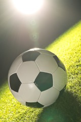 Single soccer ball on green grass lawn background with lensflare from stadium light
