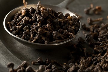 Heap of raw, dried cinnamon blossom buds spice on metal plate with metal scoop on rustic black table background