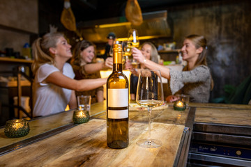 Girls drinking wine at a bar and clinking their glasses with a bottle of wine in the foreground