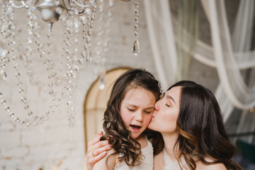 Mother and daughter hugging and playing together. Pretty little girl and beautiful woman. Girls in lace dresses playing in decorated room. Family weekend, beauty day, having fun, love concept.