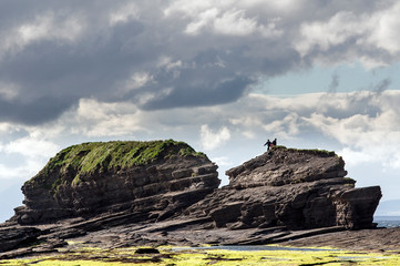 two people climbing a large beach rock in silhouette