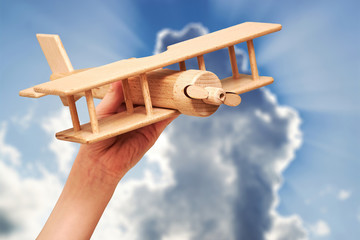 A wooden biplane plane soars into the cloudy skies. Toy in a children's hand. Dramatic sky with...